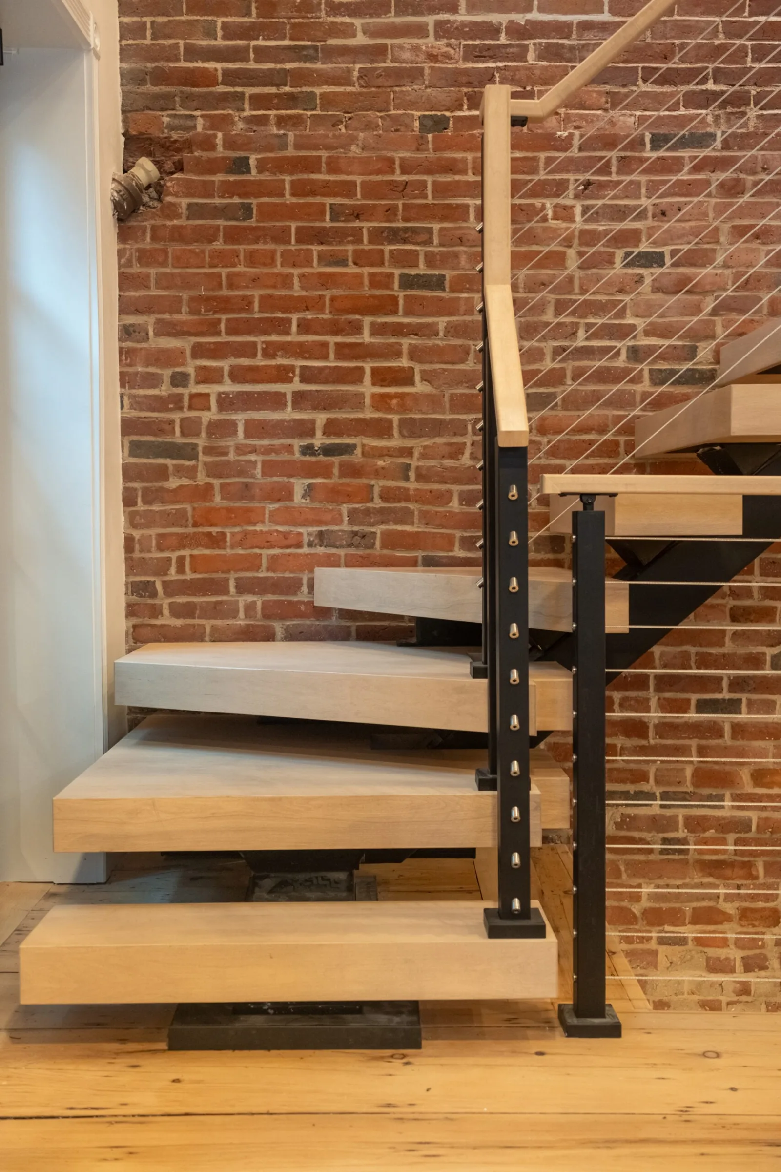 Lower treads and black post standing against an exposed brick wall