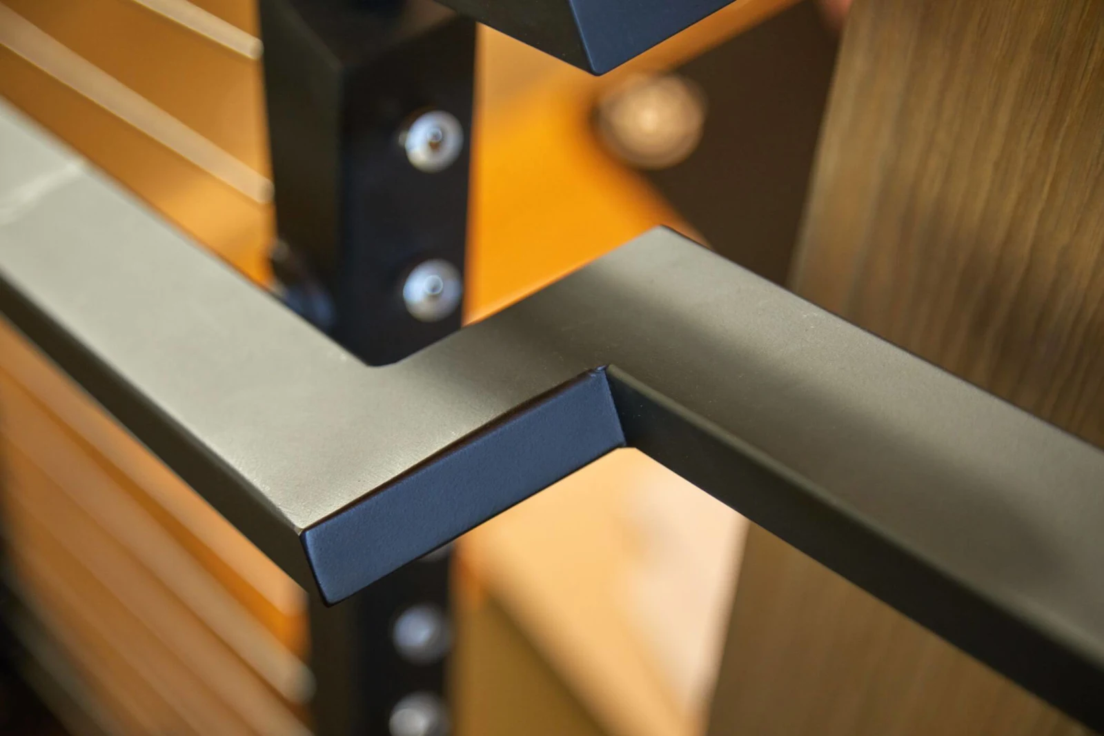 Dark handrail joint and post detail in front of wood paneling