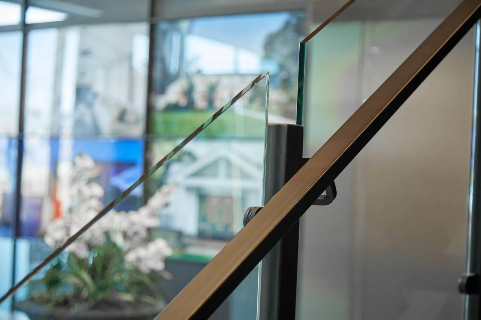 Close view of a wood-toned top rail meeting a glass panel clamp
