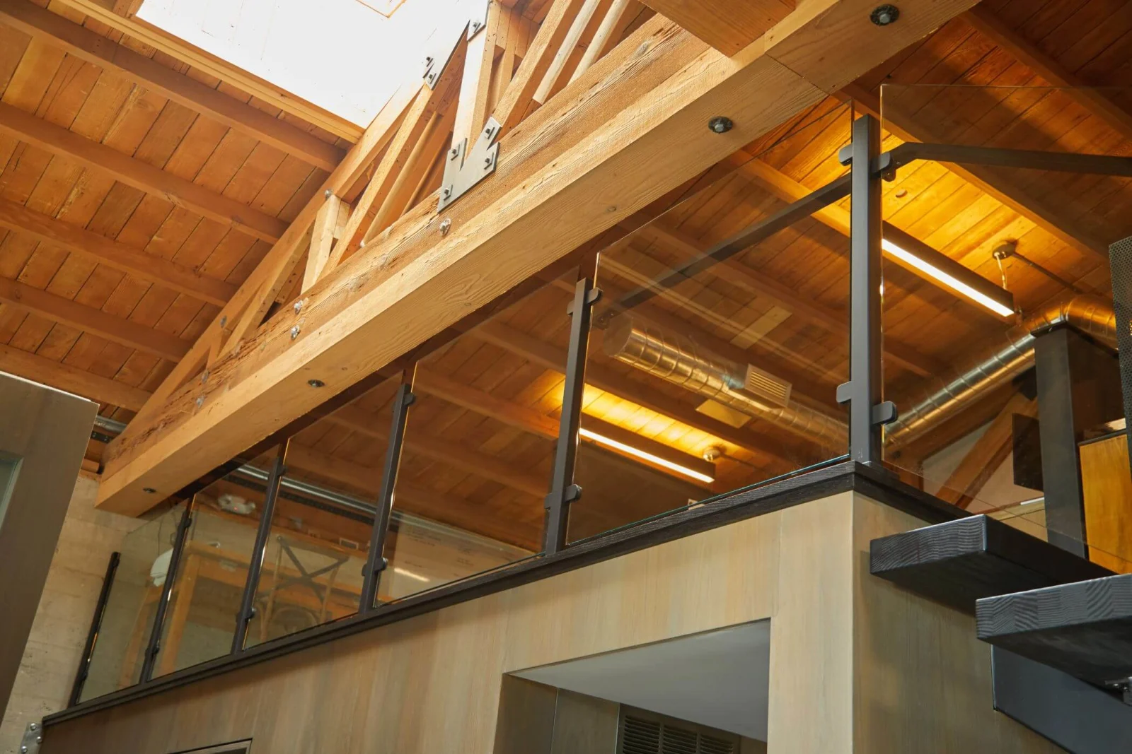Loft glass railing and dark clamps seen from below against wood rafters