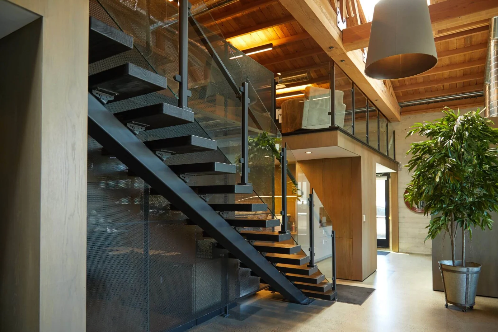 Dark steel floating stair with glass railing under a wood plank ceiling