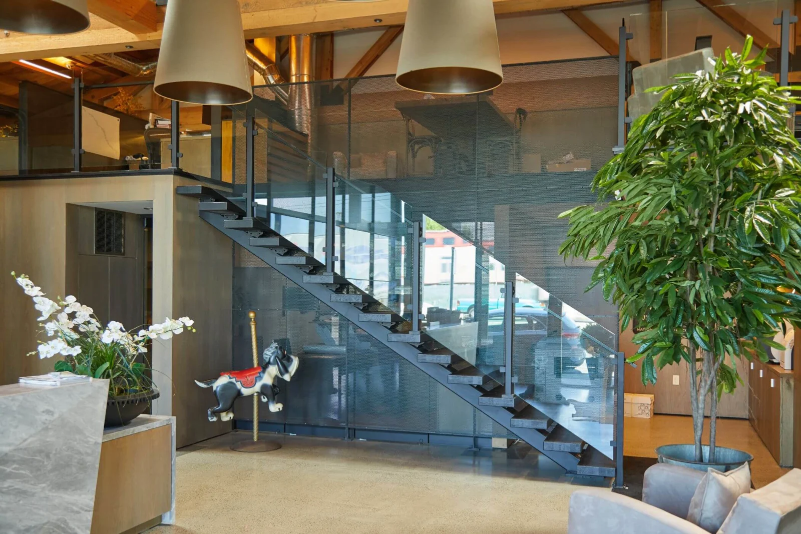 Tinted glass railing on a dark stair under exposed trusses and drum pendants
