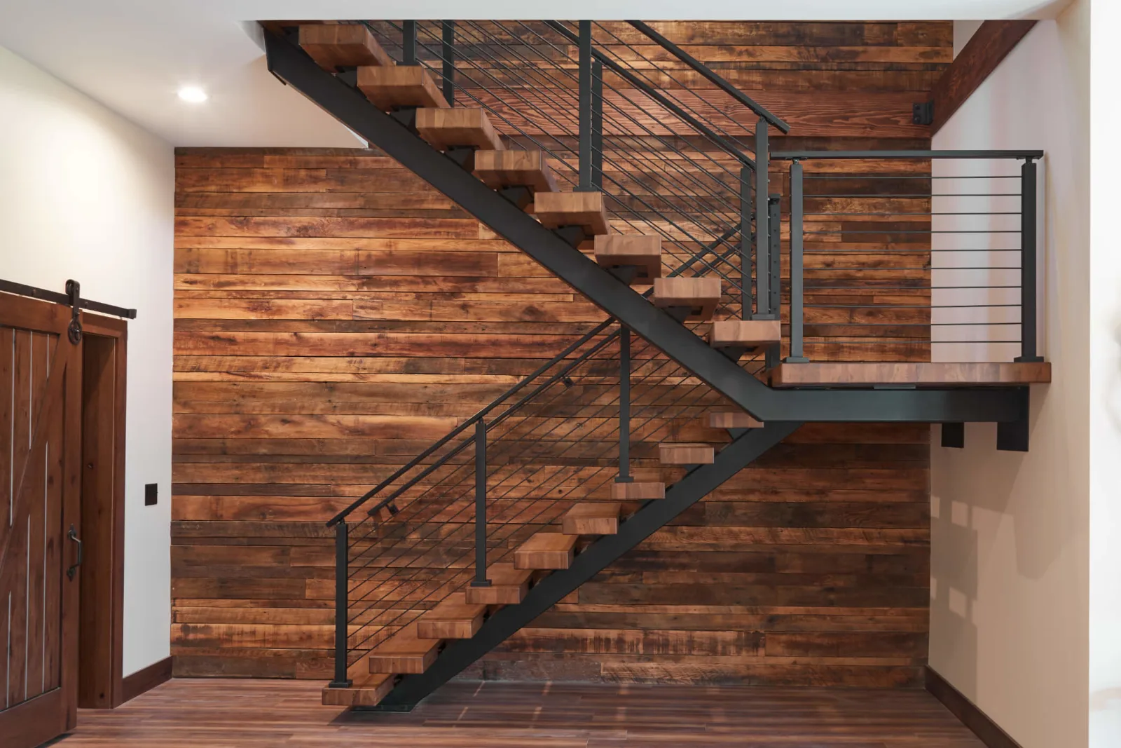 Reclaimed plank wall frames a stair and landing with black posts and thin cables