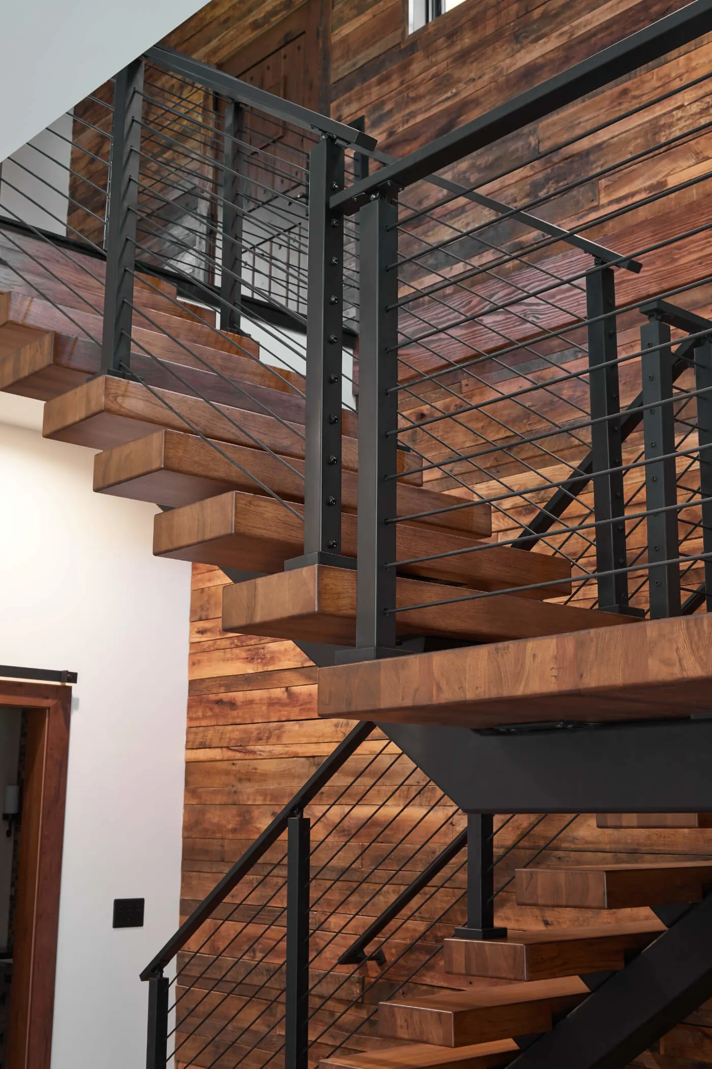 Floating stair against a reclaimed plank wall with black stringer and cable railing