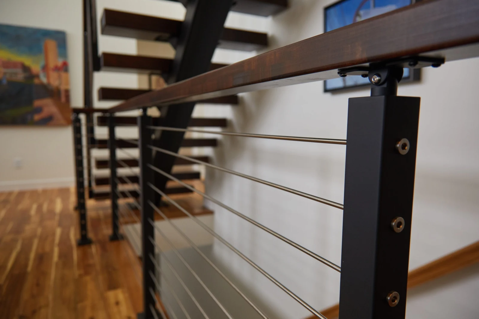Wood handrail meeting a black post above horizontal rod infill