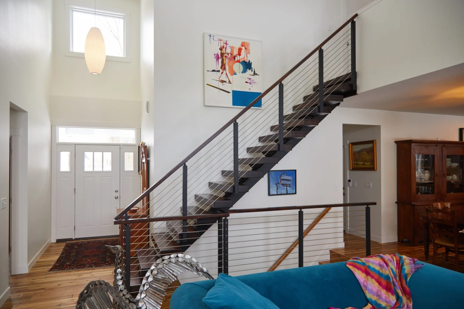 Two-story entry stair with rod railing rising past artwork toward a white front door