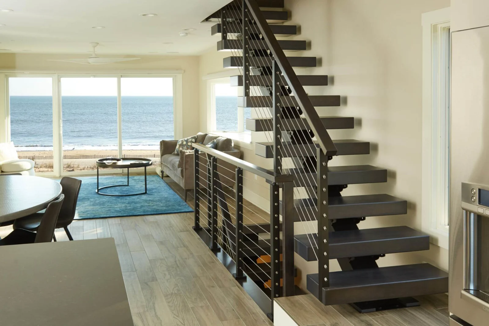 Dark treads and cable railing in a beach house with ocean framed by sliding doors