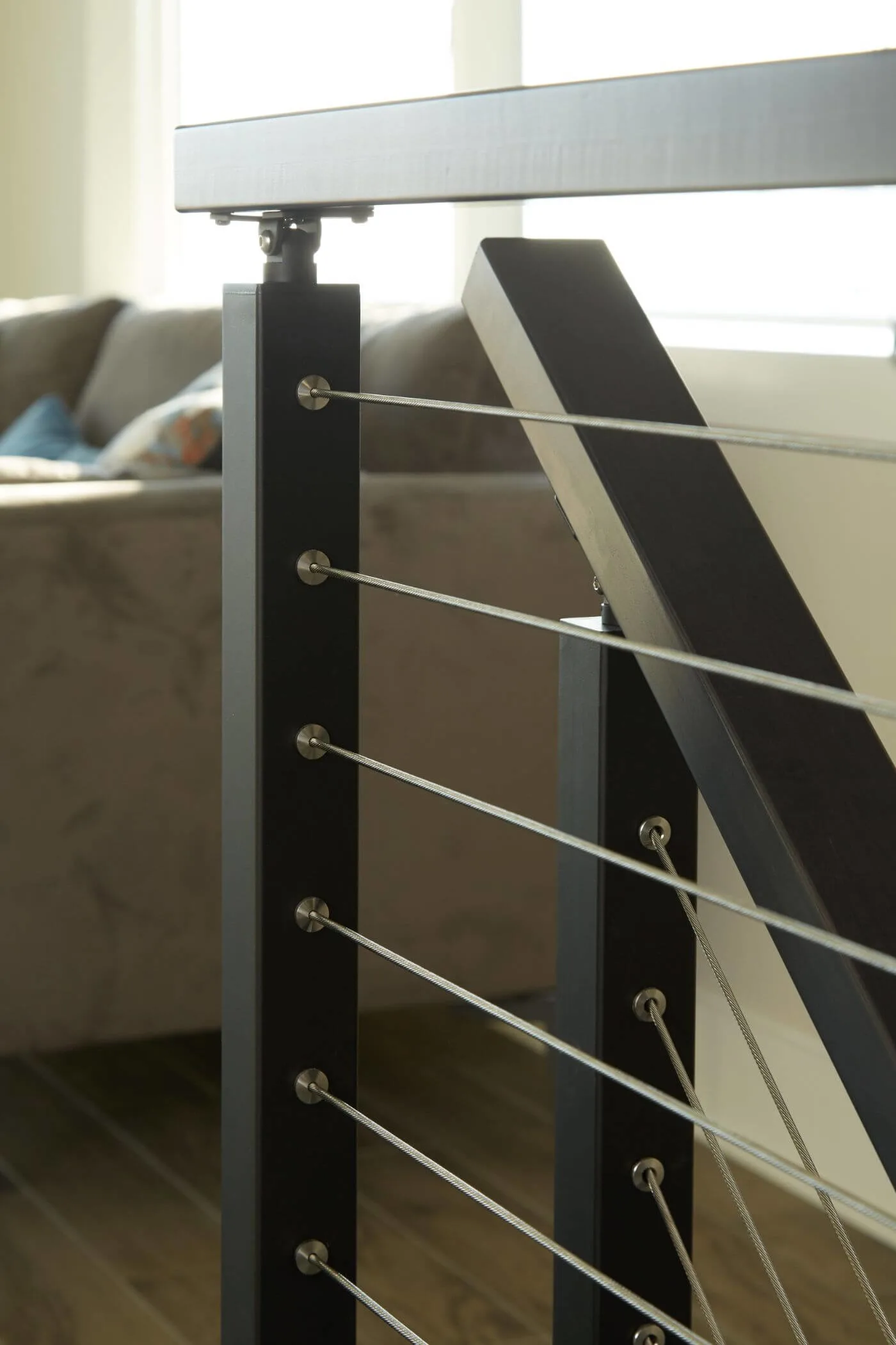 Cable railing post and metal top rail with a sofa beyond