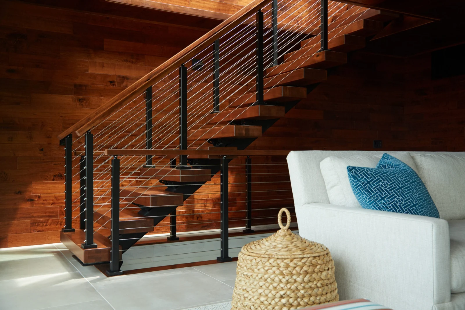 Warm wood-paneled wall behind a stair with black posts, cables and a wood top rail