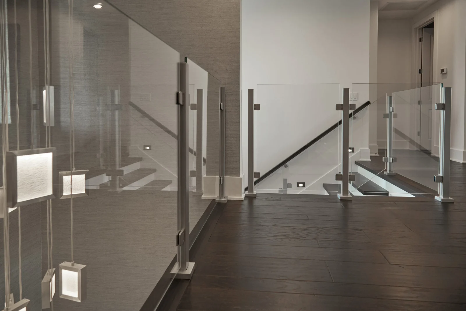 Glass railing panels on metal posts edging a stairwell over dark flooring