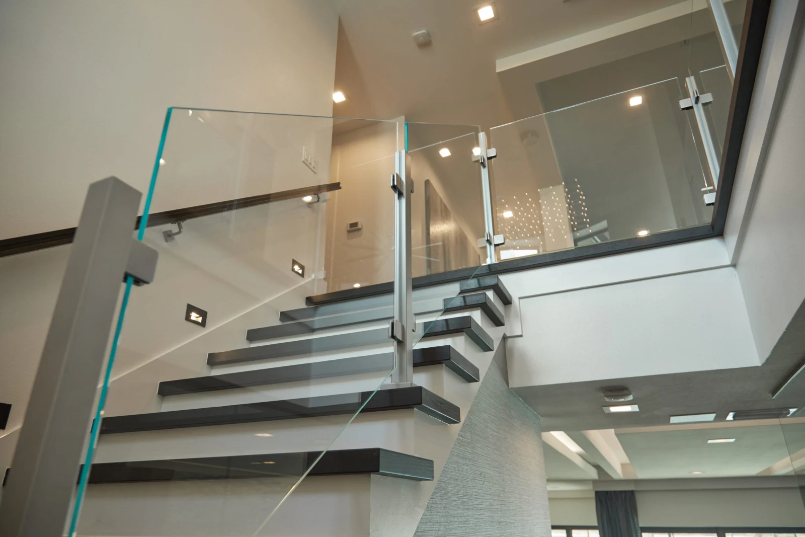 Looking up at dark treads and glass railing inside a tall glazed space
