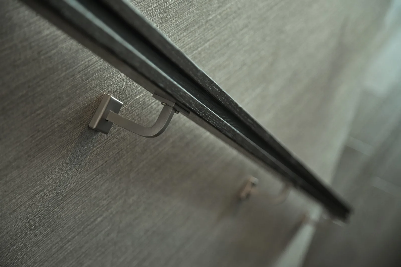 Close bracket detail holding a dark wall-mounted handrail against the wall