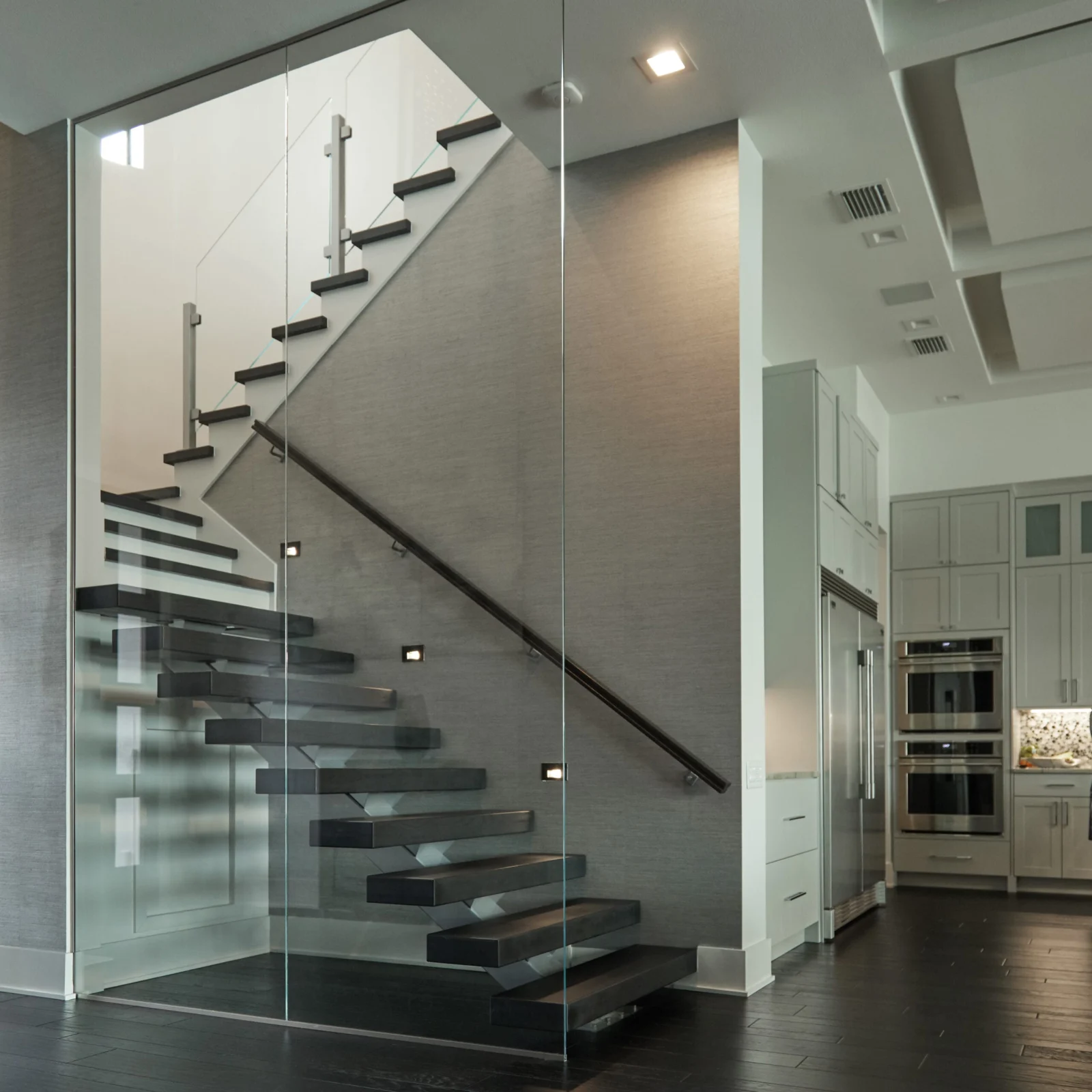 Stair and glass partition beside the kitchen with dark plank flooring