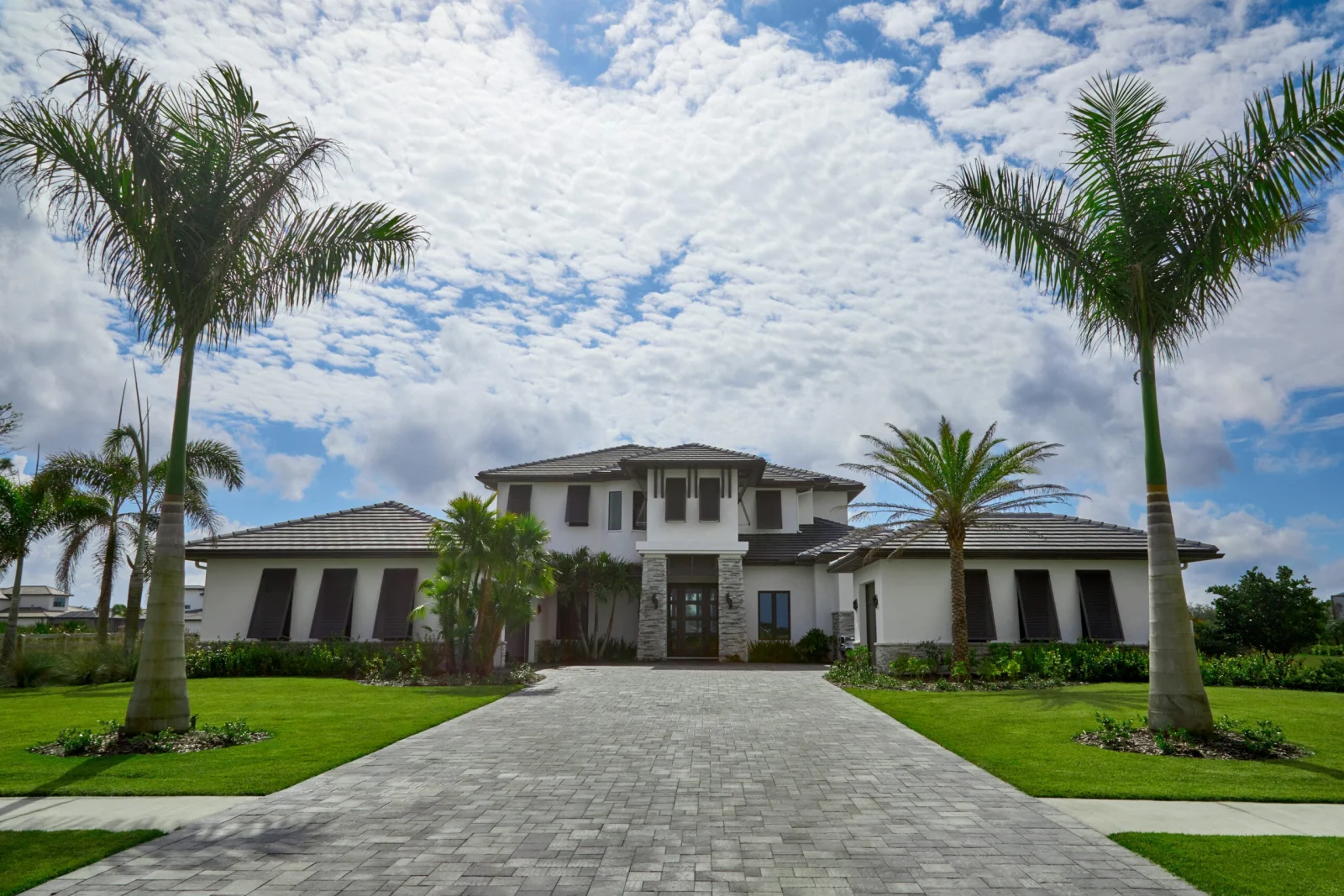 Two-story house front with palm trees and a paver driveway
