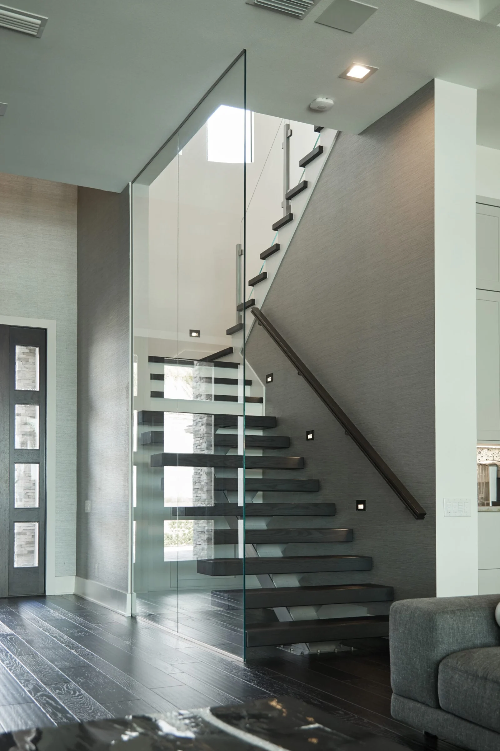 Dark treads behind a glass wall with a handrail tracking the rise