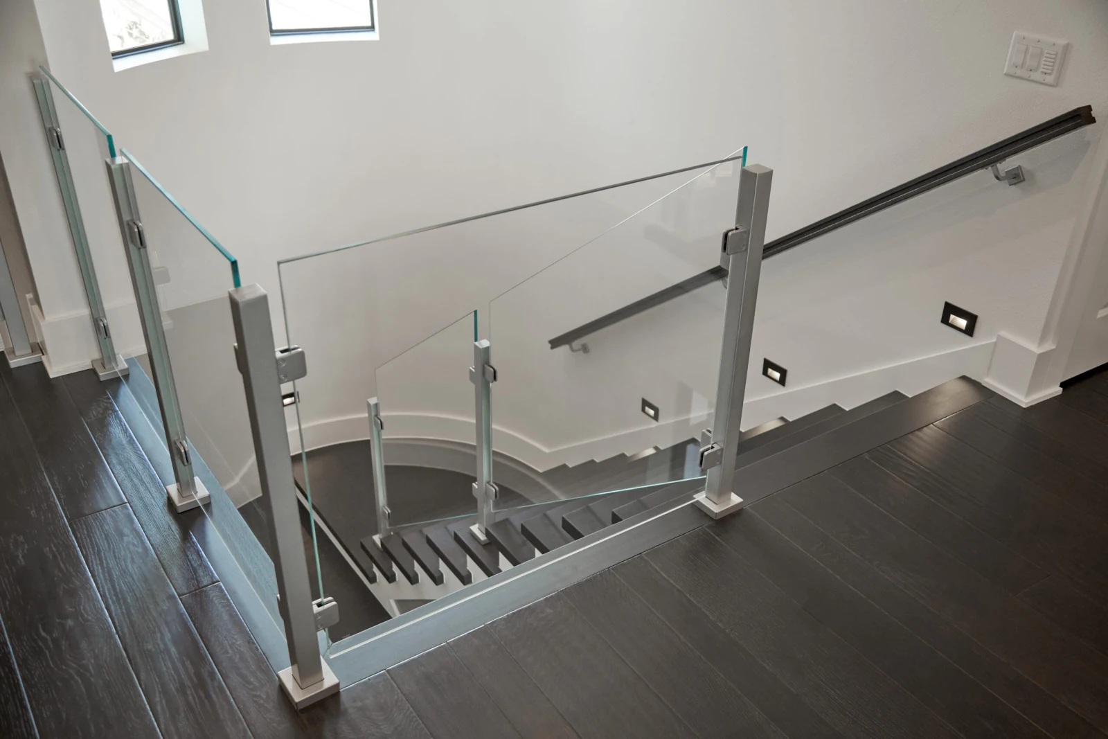 Glass railing wrapping the stair opening with a wall-mounted handrail