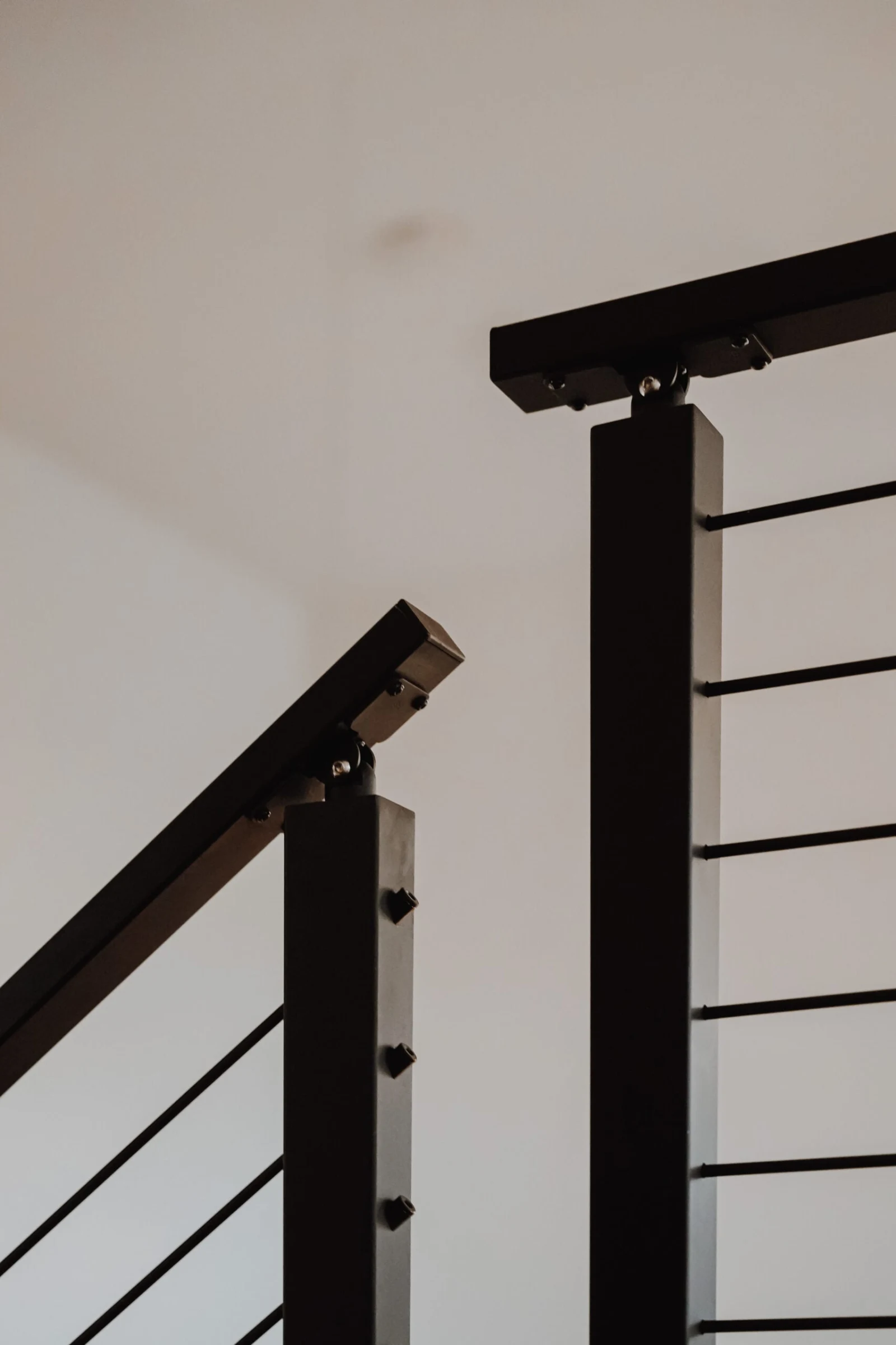 Looking up at black railing posts and angled top rails meeting above a white wall