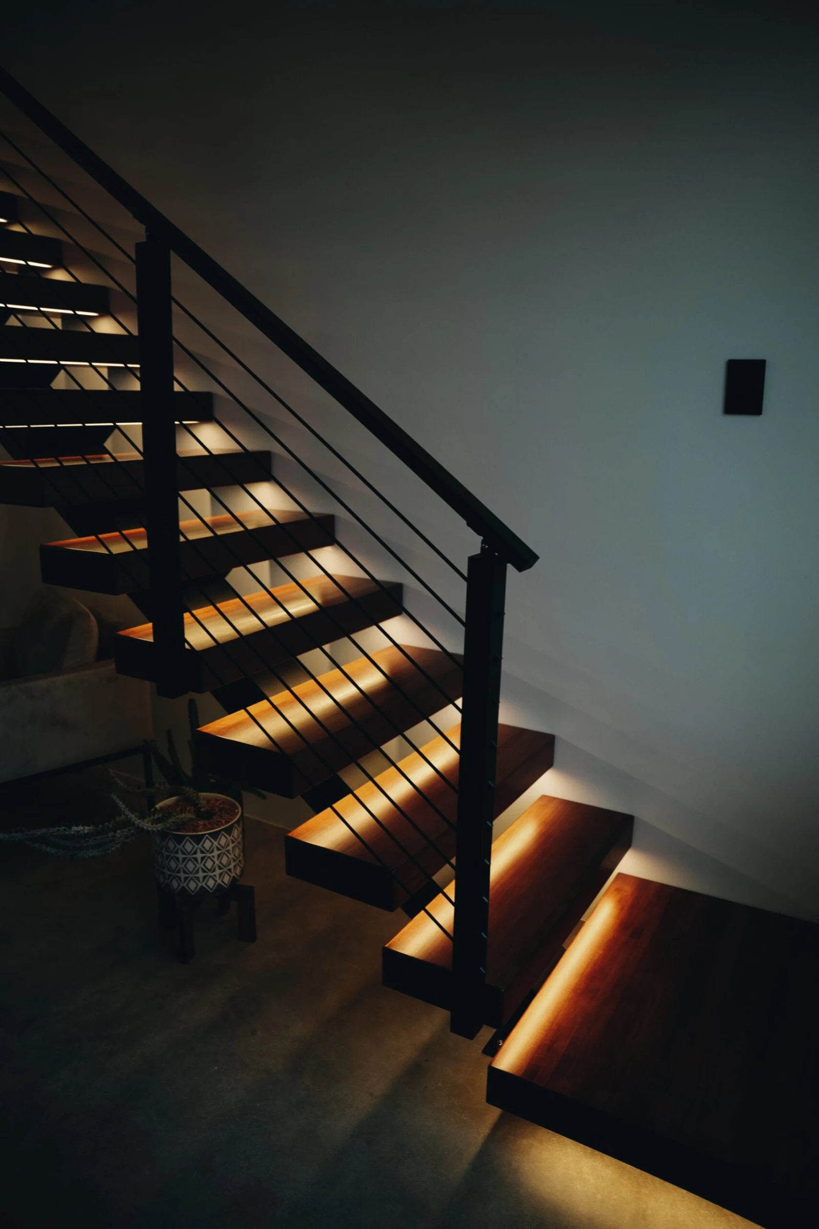 Dimly lit room where the full flight glows from under-tread lighting against a dark wall