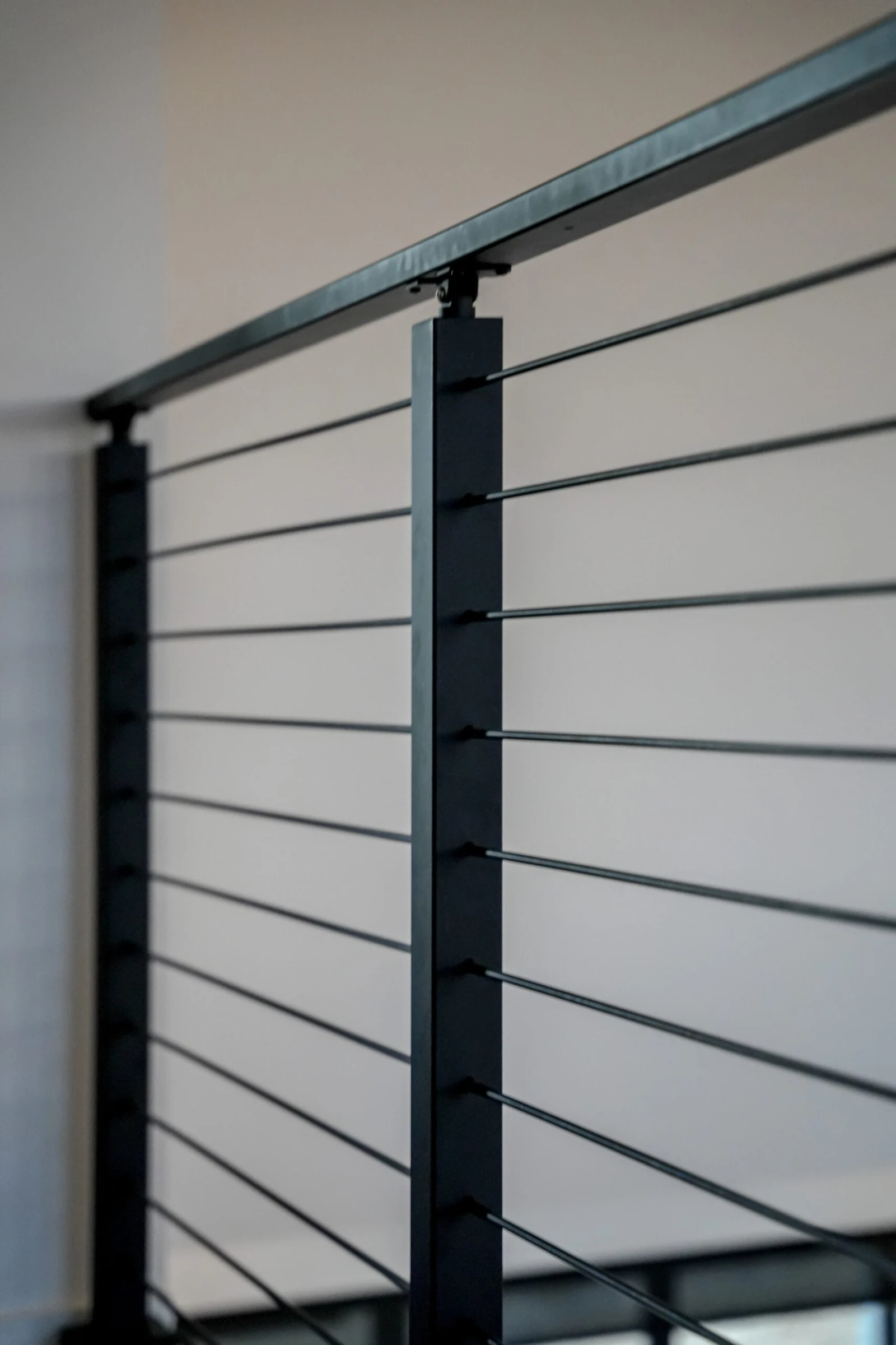 Balcony run of horizontal rod infill between black posts along a bright upper landing