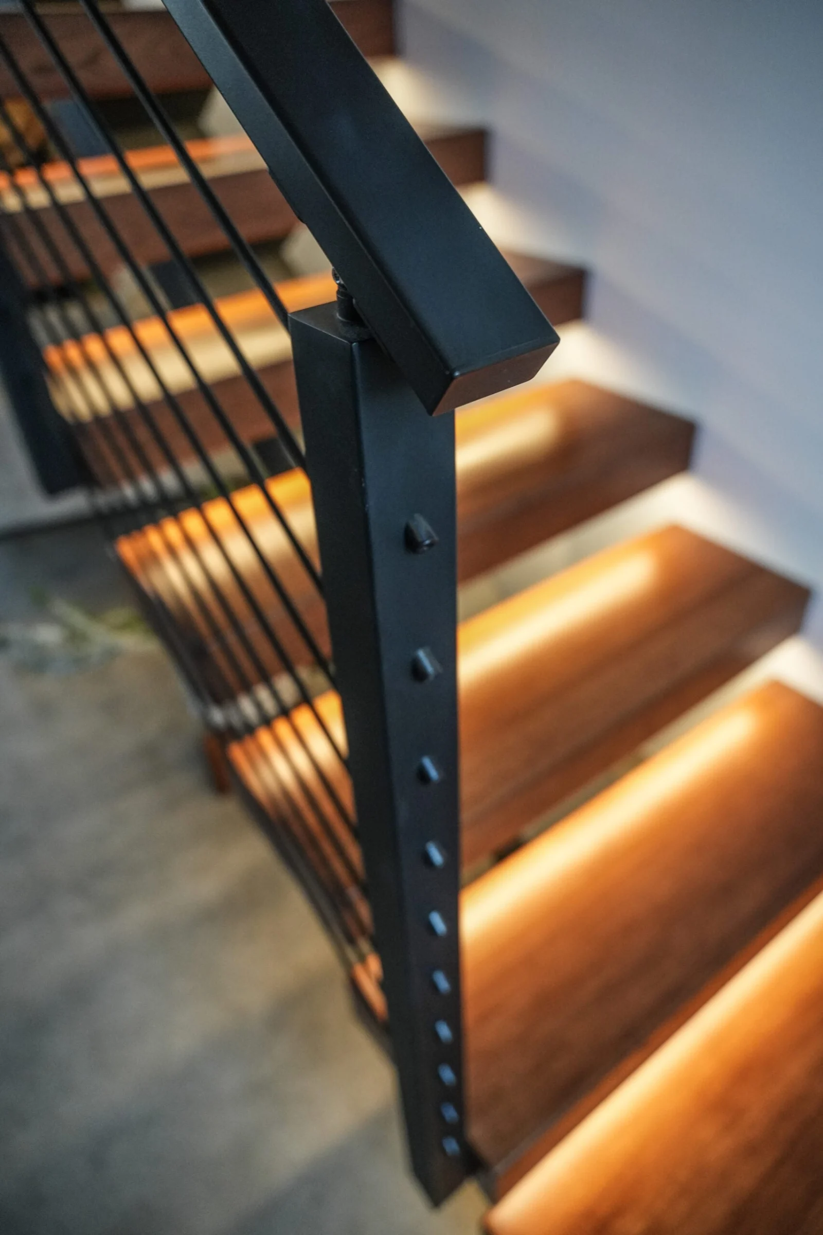 Looking down a black post to warm strip lighting glowing under each floating tread