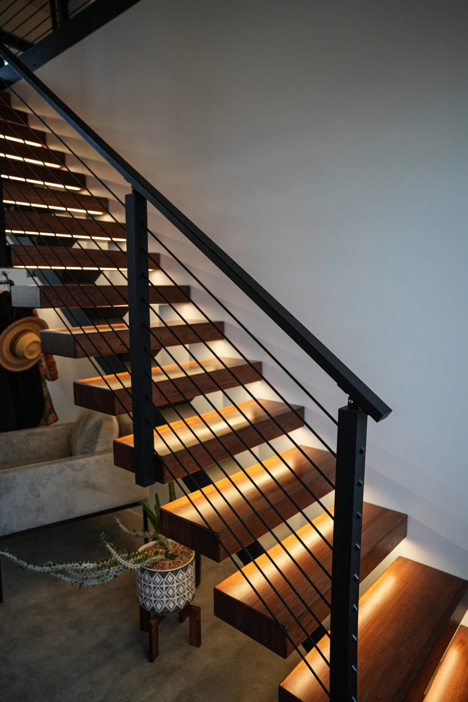 Flight seen from the room below, lit treads climbing past a plant and armchair