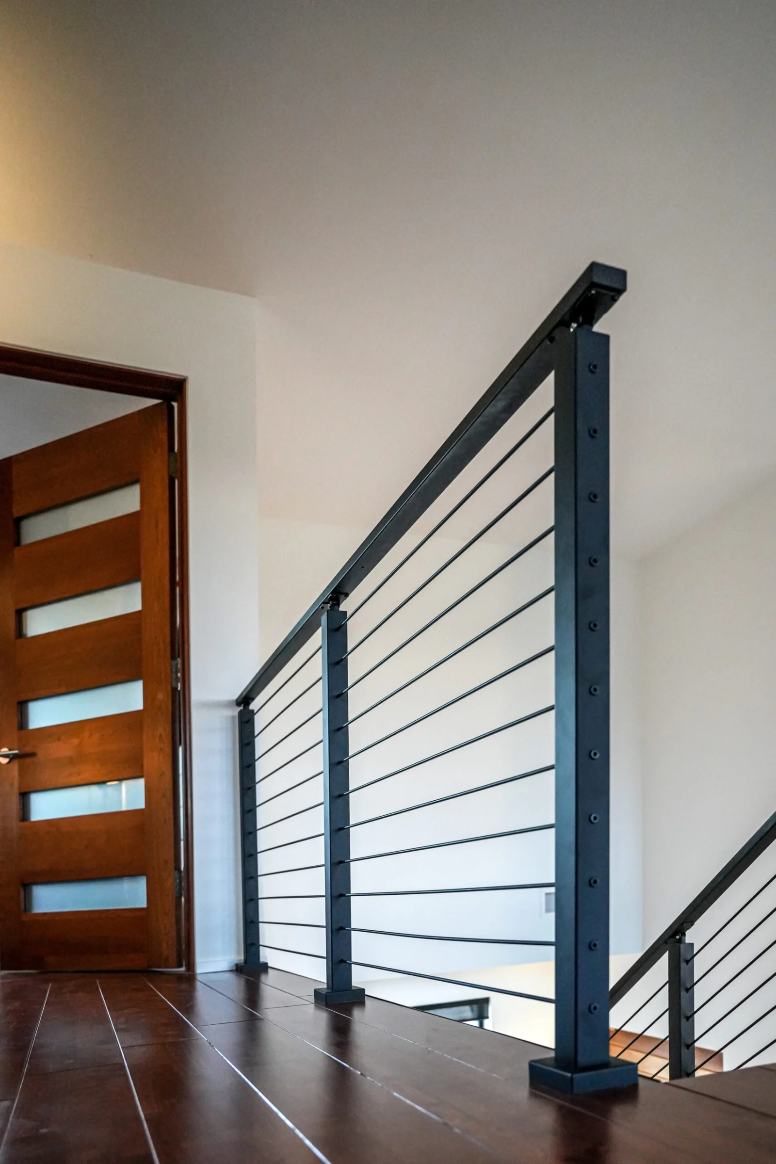 Rod railing guarding a stairwell opening beside a glass-panel door on tile flooring