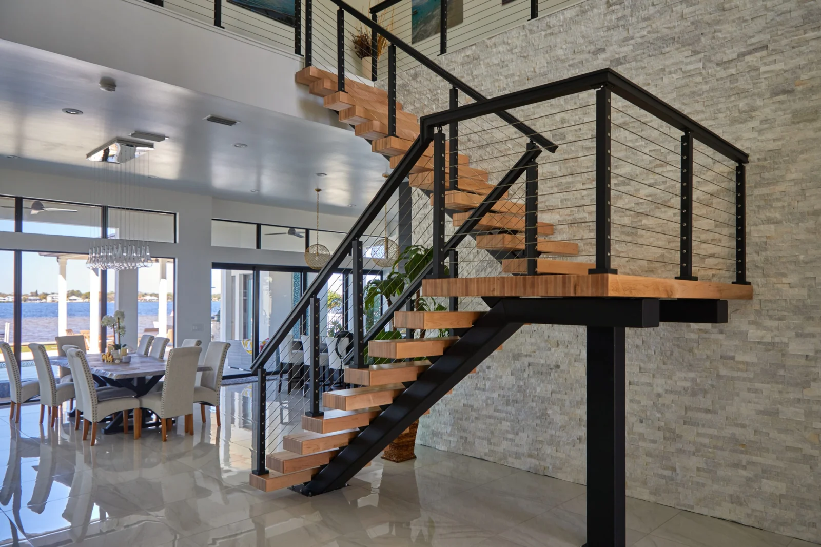 Stacked stone wall behind a stair and landing overlooking a dining room and water