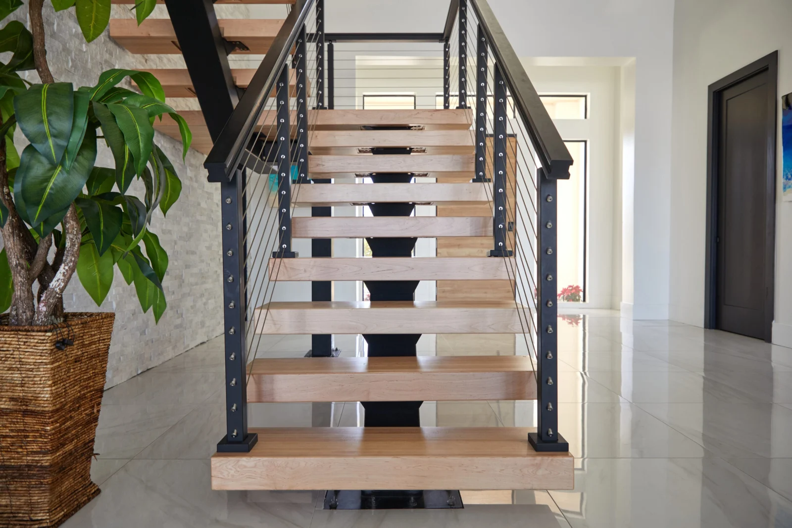 Front view of the light wood treads climbing between black posts beside a potted plant