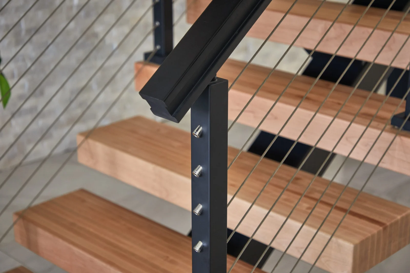Close detail of a black post and top rail with tensioned cables over treads