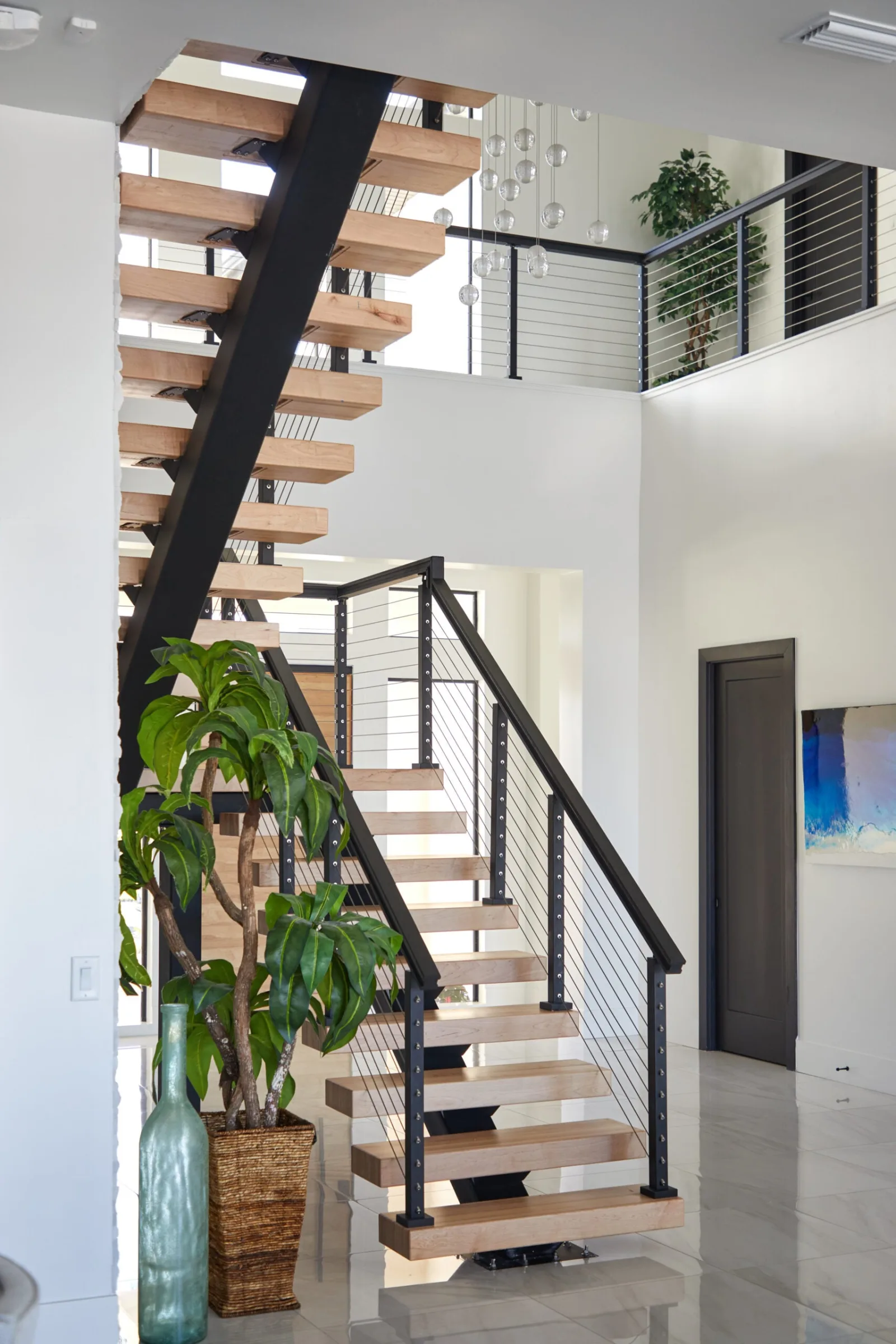 Full-height view of the stair rising to a cable-railed balcony under a tall ceiling
