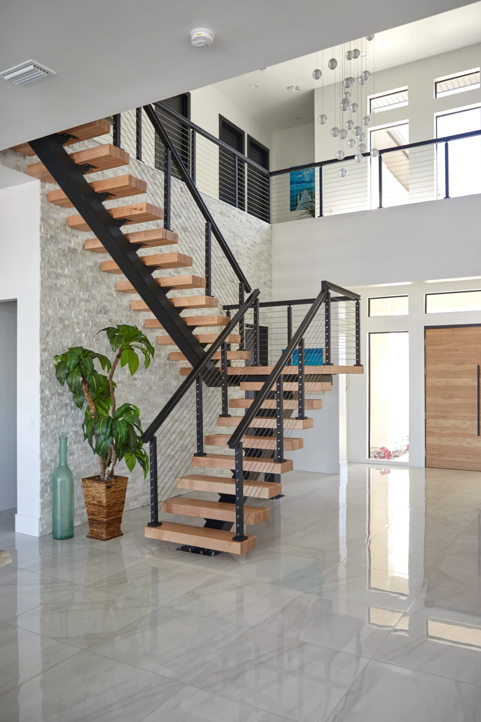 Entry hall with the stair set against a stacked stone wall beside a bright doorway