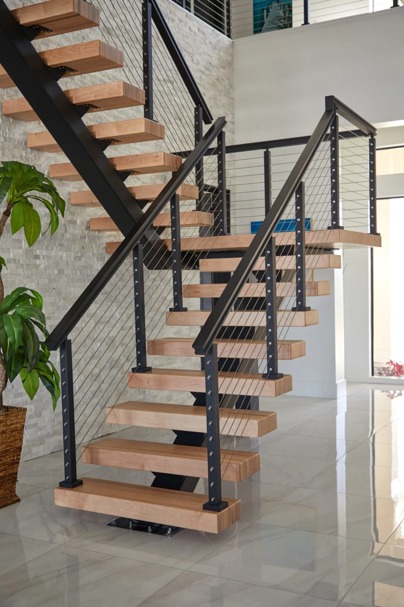 Stair viewed head-on, cable railing wrapping the landing above the stacked stone wall