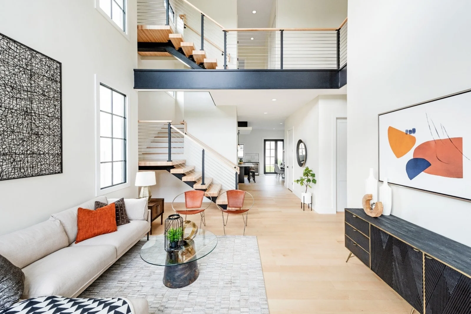 Bright two-story living room with a cable railing balcony above a low white sofa