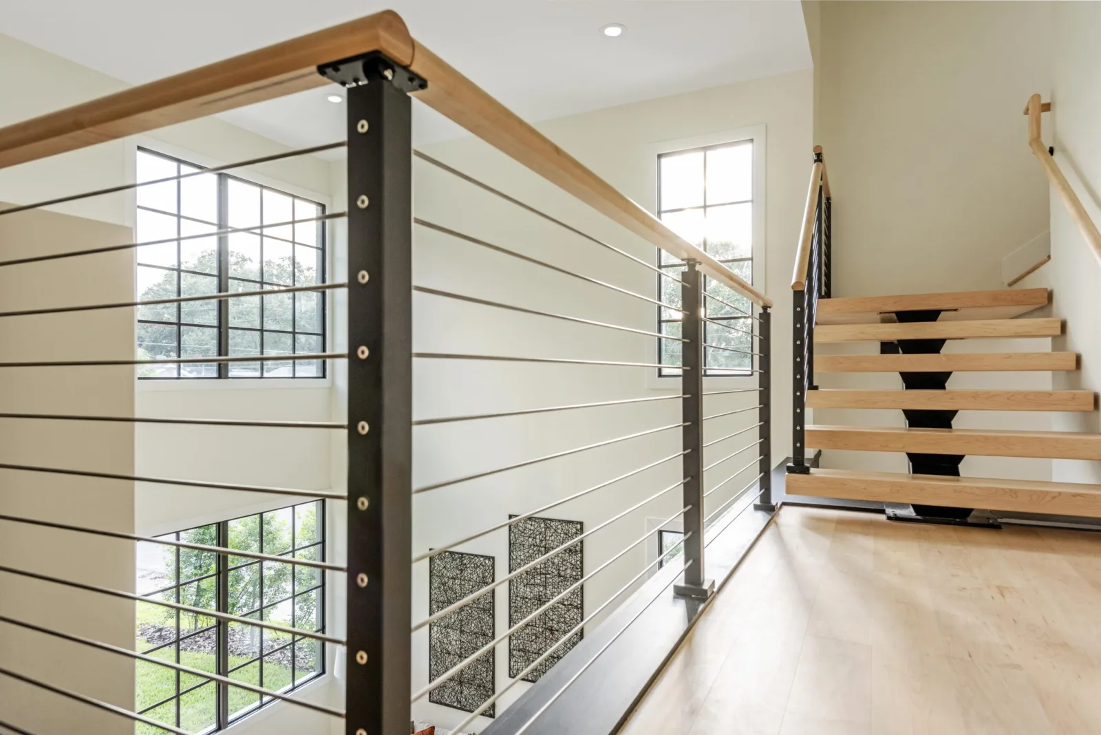 Upper hallway lined with stainless rod railing under a light wood top rail
