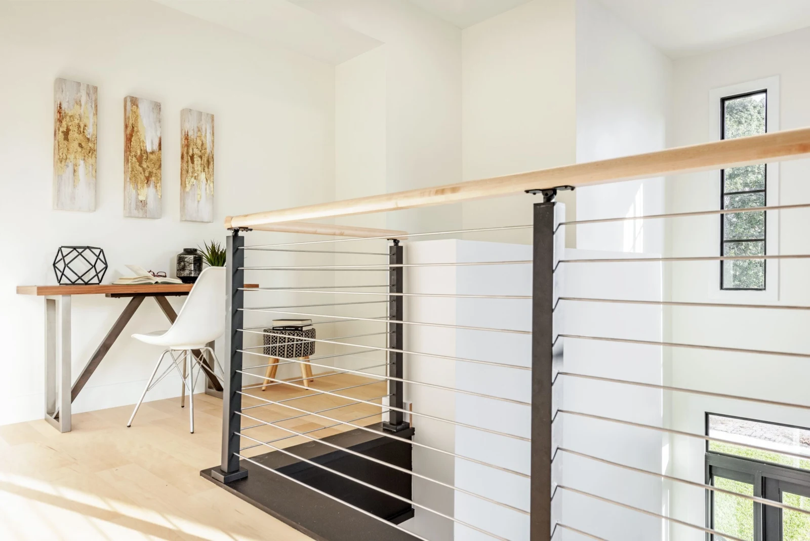 Rod railing edging a loft workspace with a desk and molded chair beyond