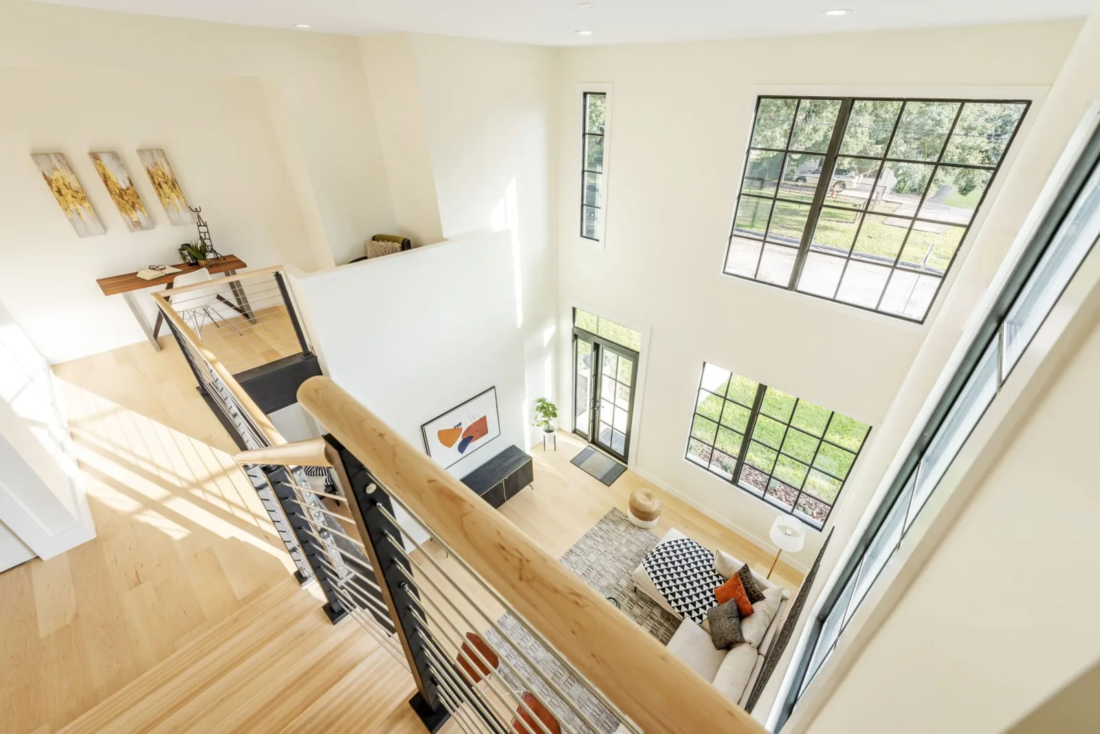 Loft overlook down into a bright double-height living room with tall grid windows