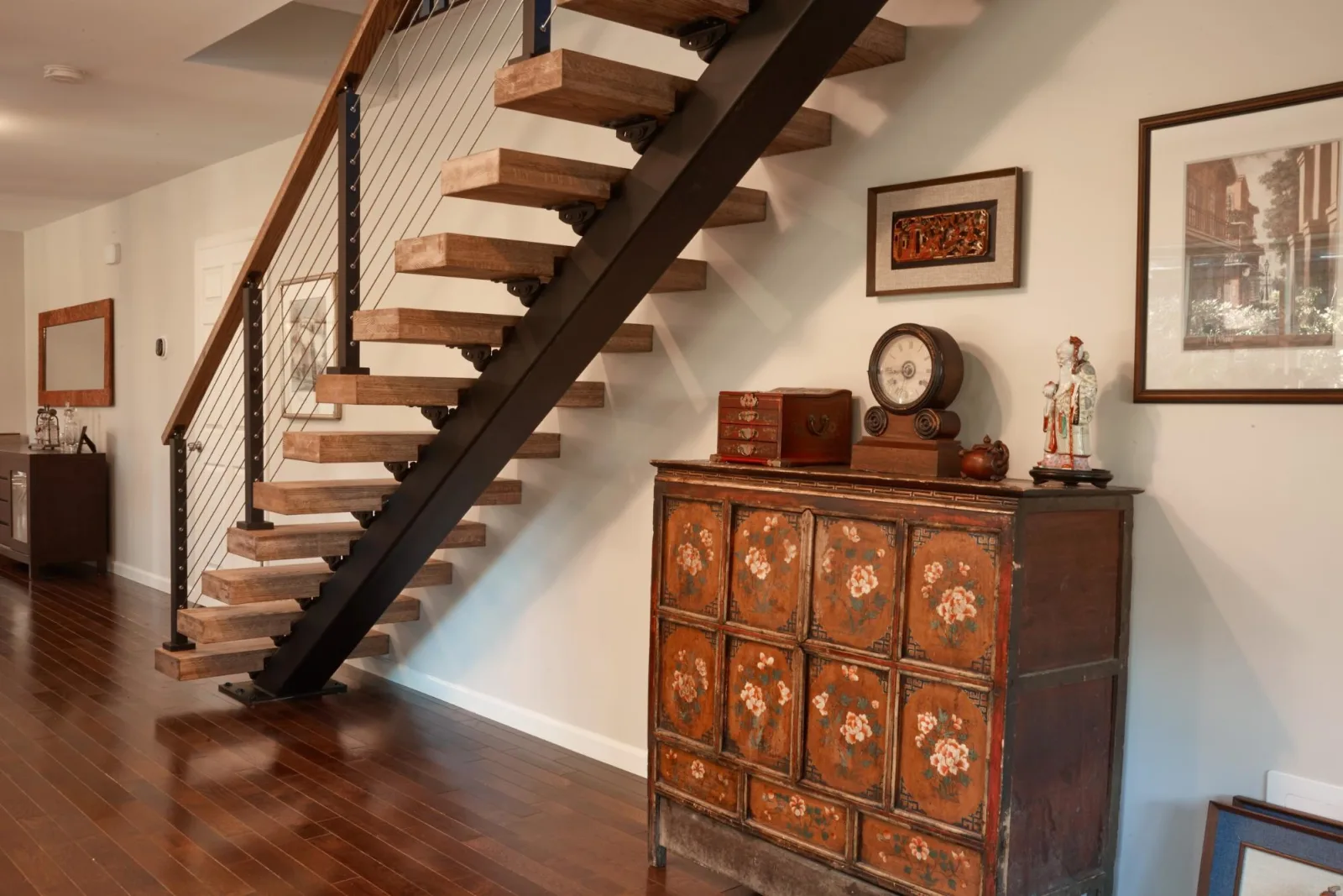 Open-riser flight on a black stringer above a painted antique cabinet and dark flooring