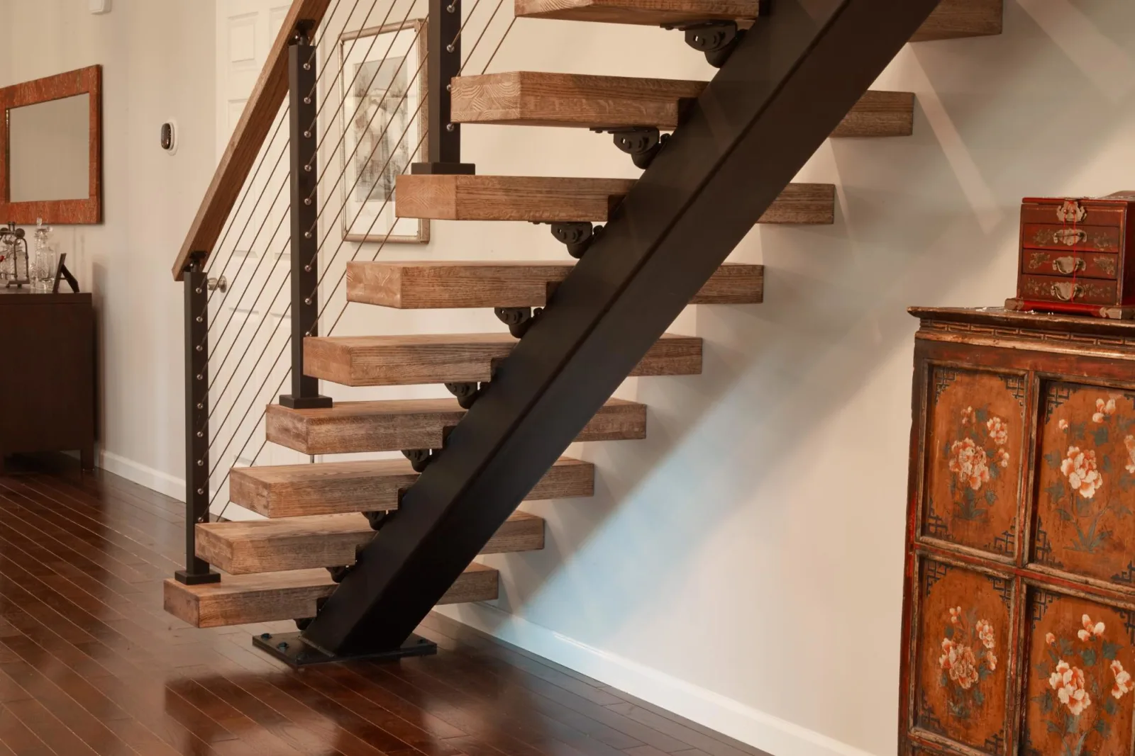 Rustic light treads on a black stringer beside an antique painted cabinet on dark flooring