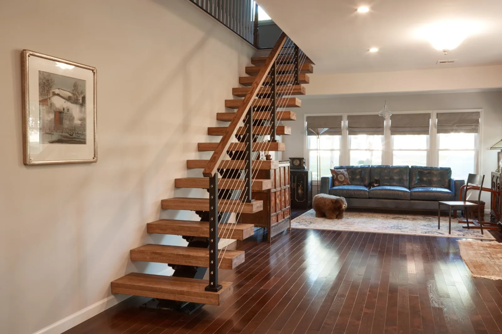 Floating stair with dark-stained treads and rod railing rising along a living room wall