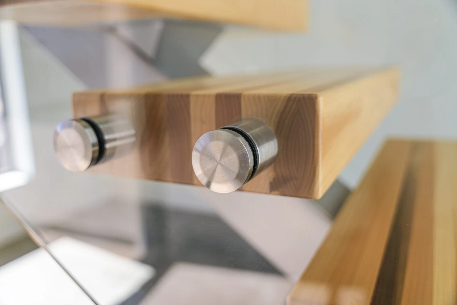 Close detail of two brushed standoff pins pinning a glass panel to a tread end