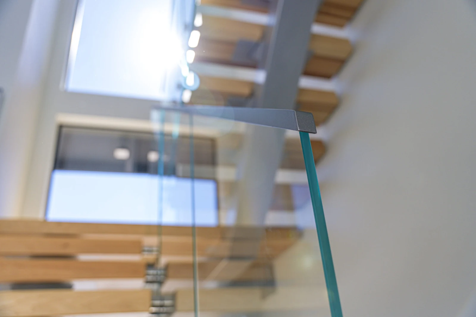 Top edge of a glass panel with its metal cap, treads blurred beyond