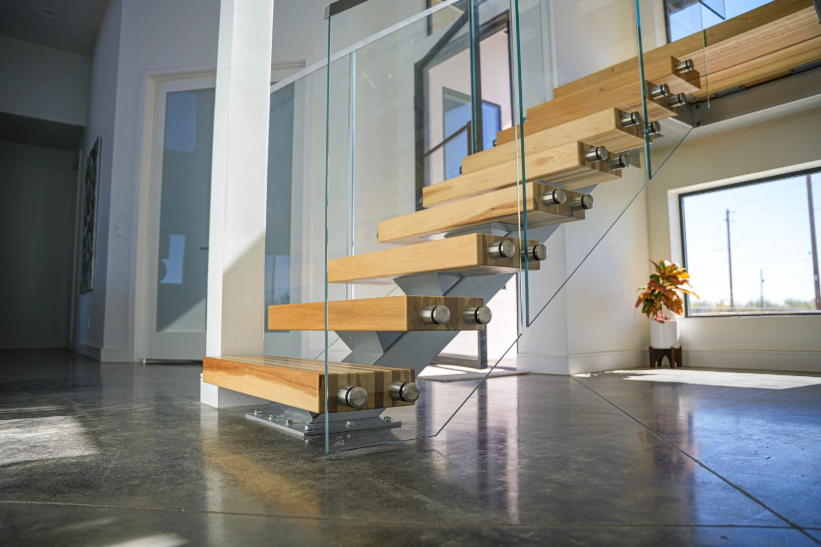 Floating stair on a silver center stringer with glass railing above polished concrete flooring