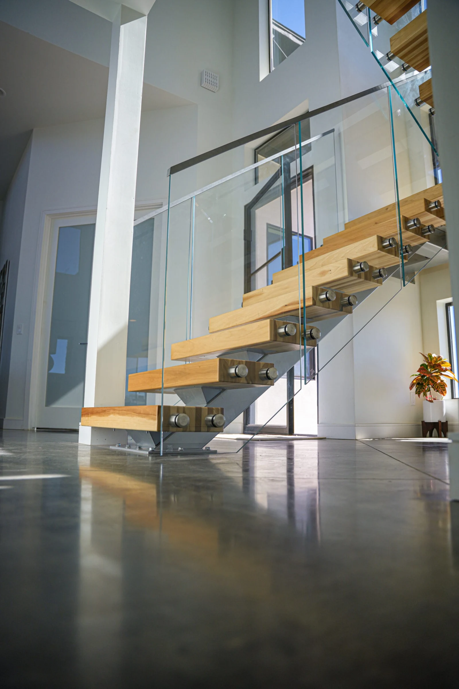 Bright hall with the stair reflected in the polished concrete floor beneath glass panels