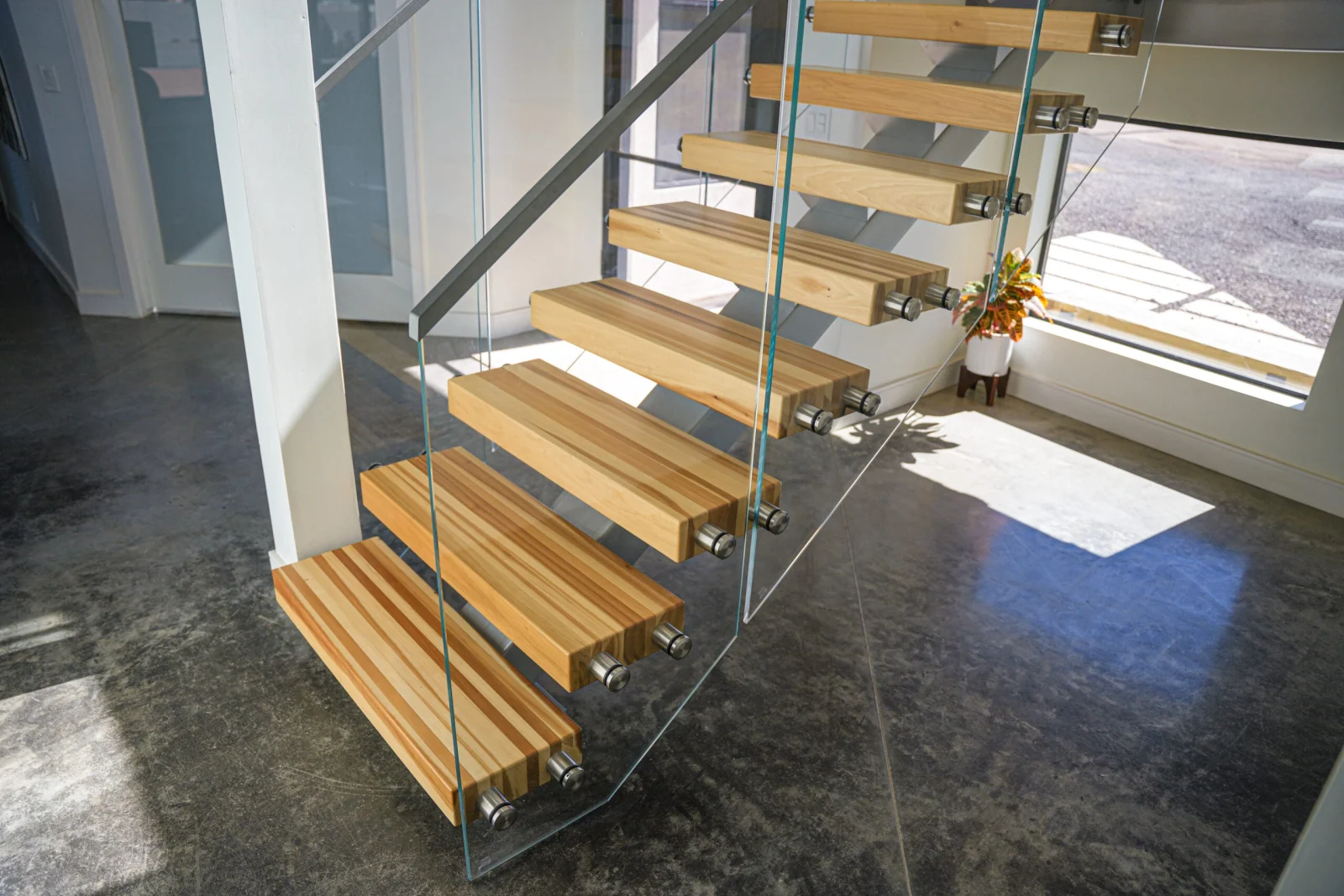 Downward view of the flight with glass panels flanking treads over gray concrete