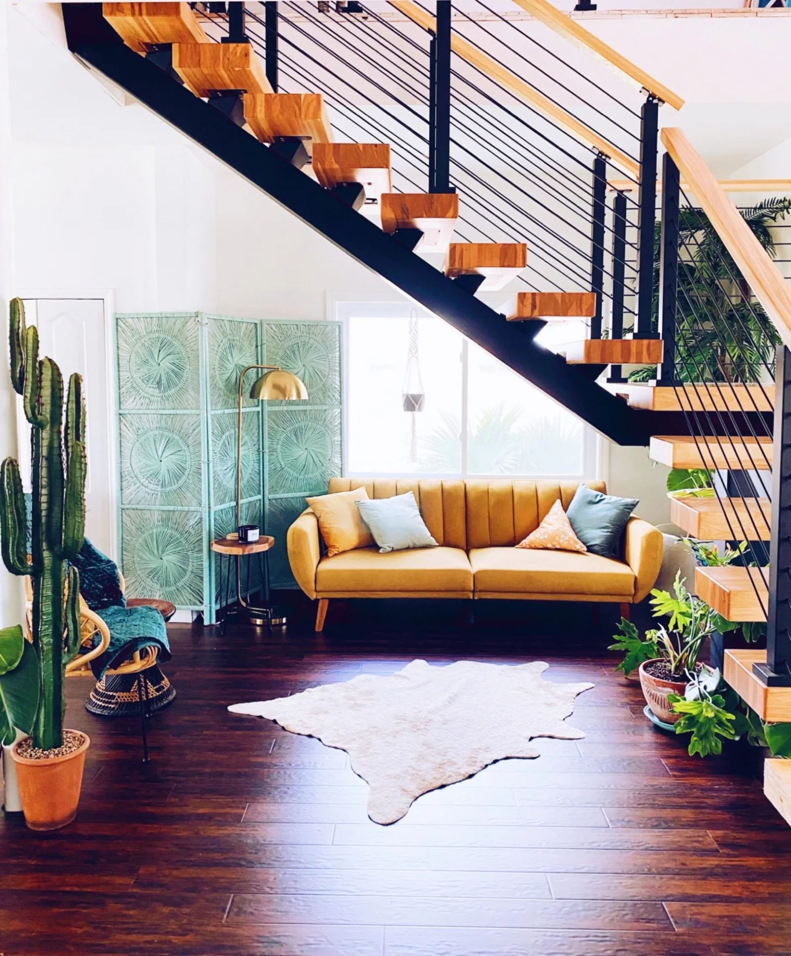 Yellow sofa and cacti tucked beneath the stair's open treads and black rod railing