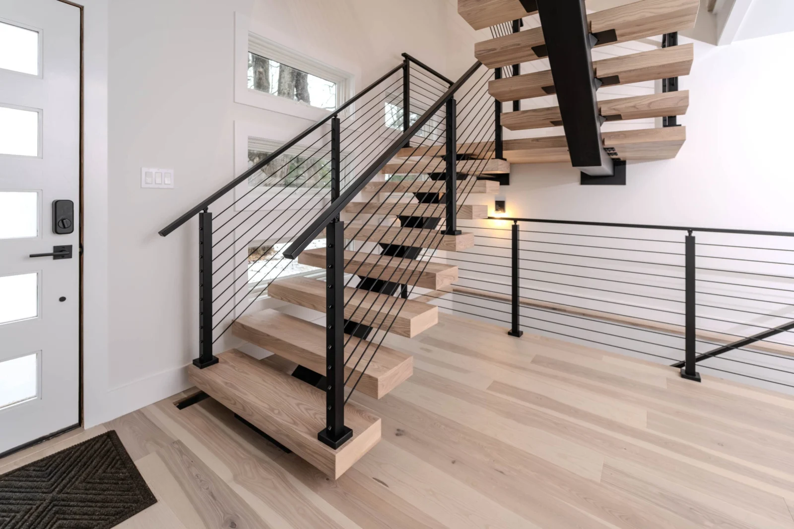 Light treads and black rod railing turn at a landing in a white plank-floored entry
