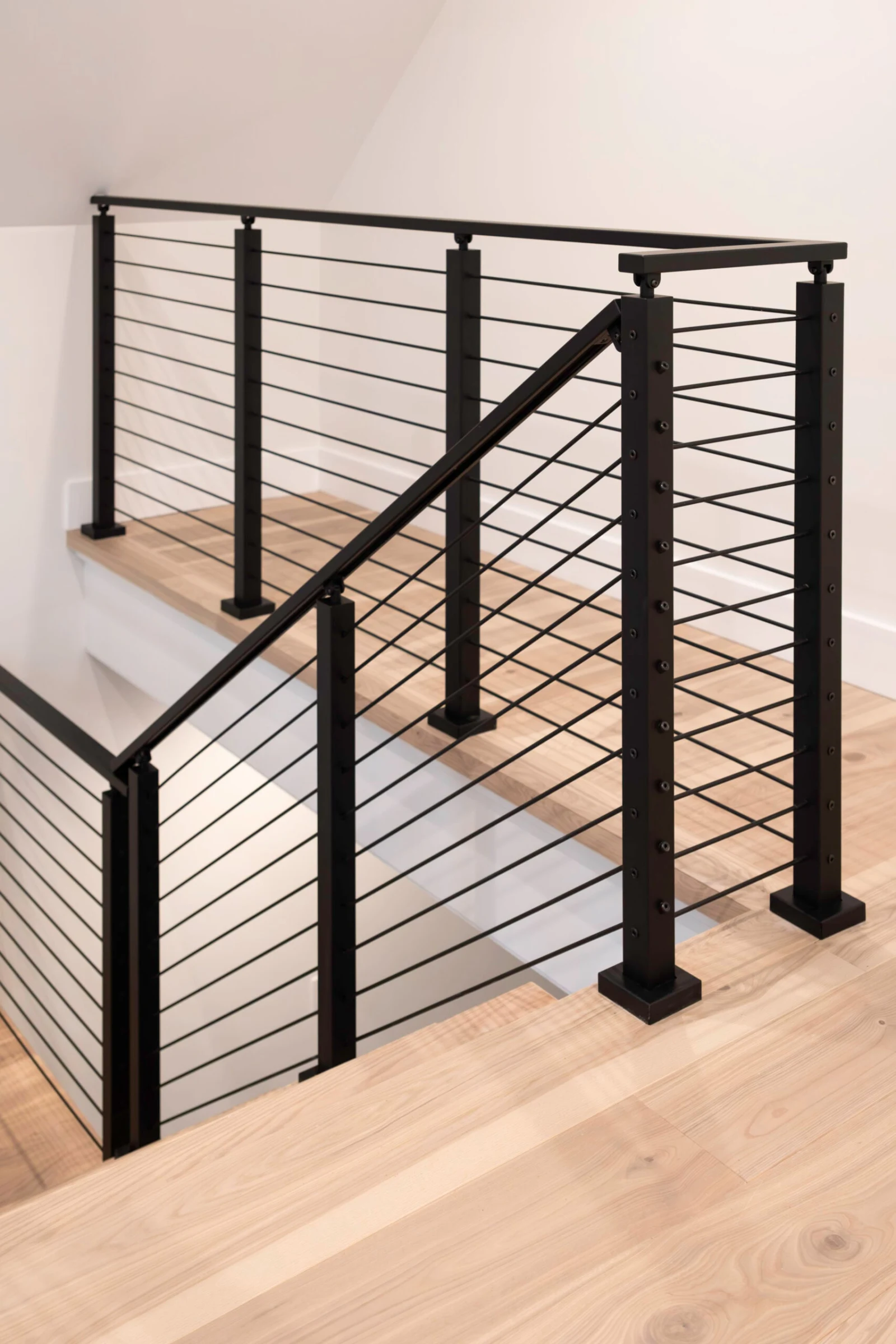 Black rod railing turning a corner at the stair opening on light plank flooring