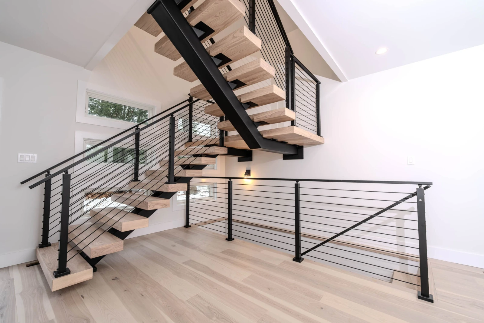 Bright room with the flight and two railing runs meeting on pale plank flooring