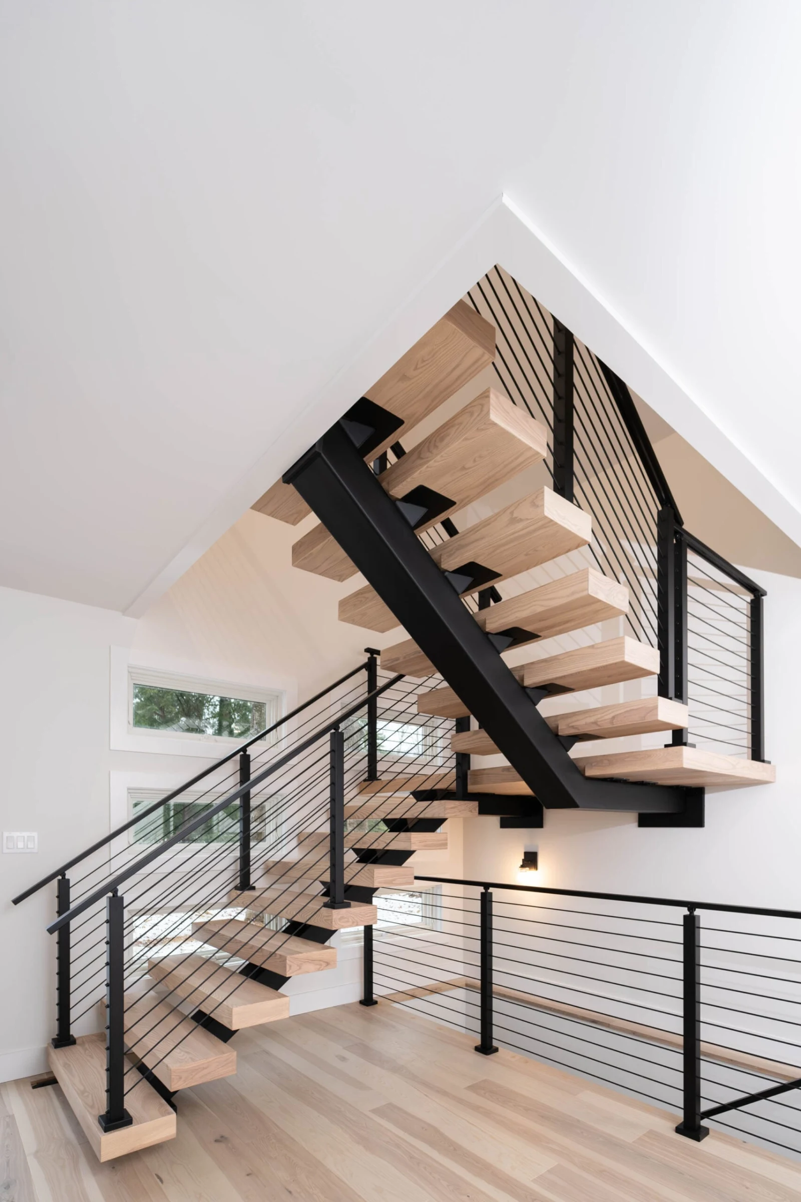 Full flight seen from below rising under a sloped ceiling past balcony rod railing