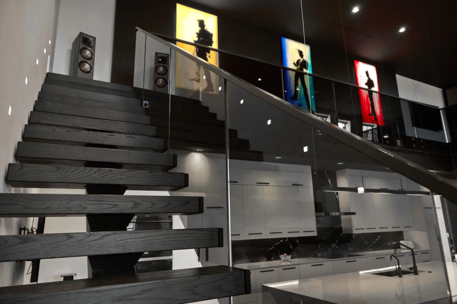 Dark treads rising behind glass panels beside the kitchen and framed art